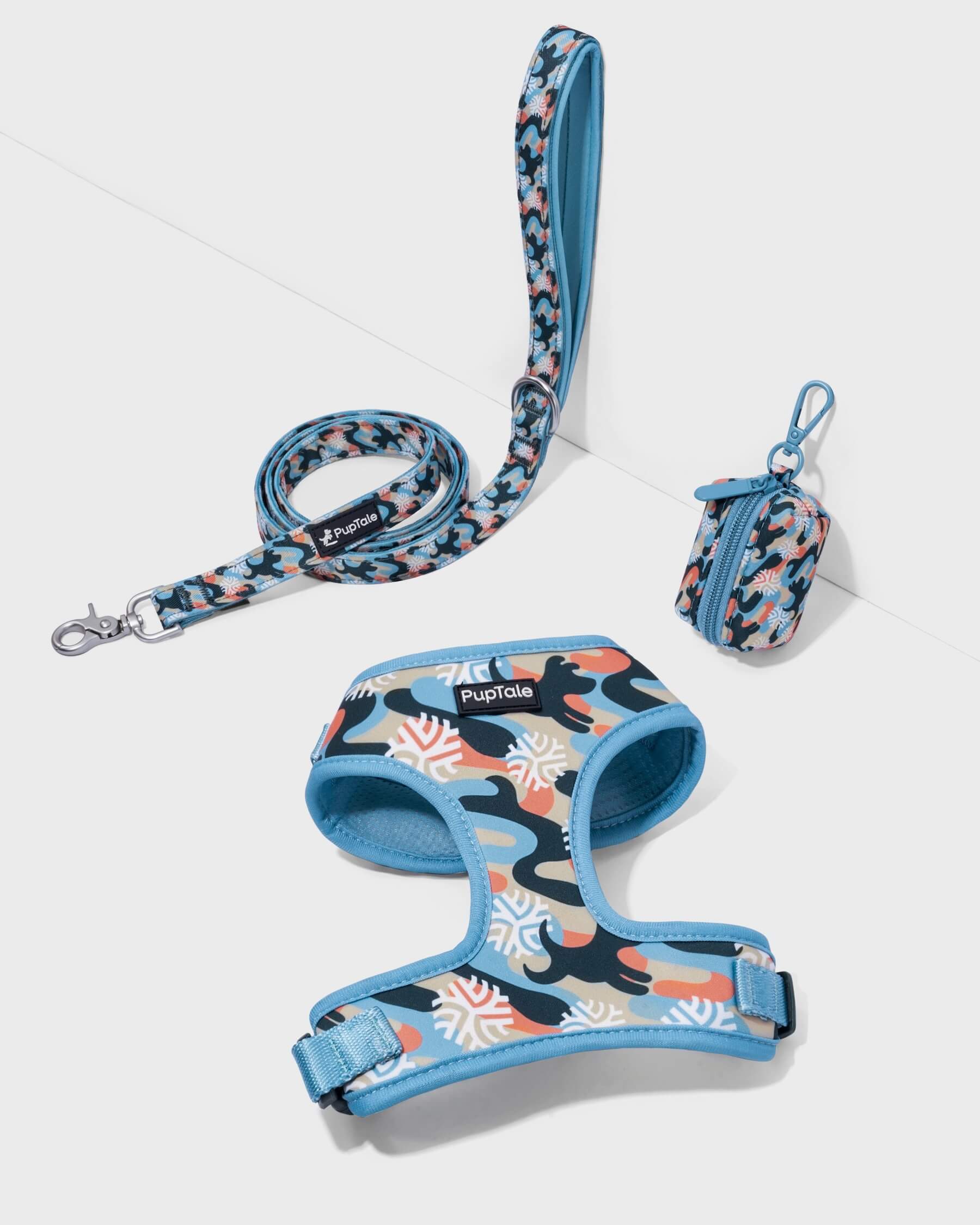 A dog harness and leash set with a winter snowflake pattern in blue and orange colors, displayed alongside a matching poop bag holder.