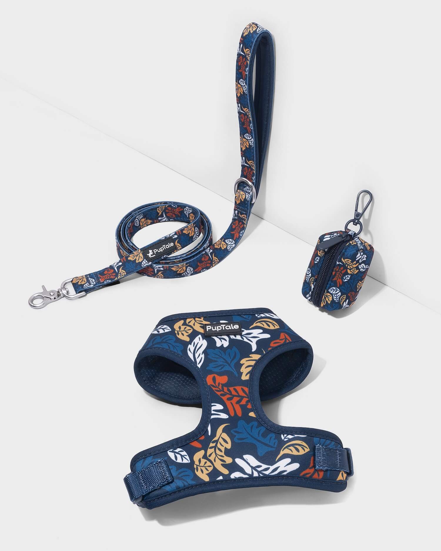 A dog harness and leash set in blue and amber fall leaf patterns, including a matching padded handle.