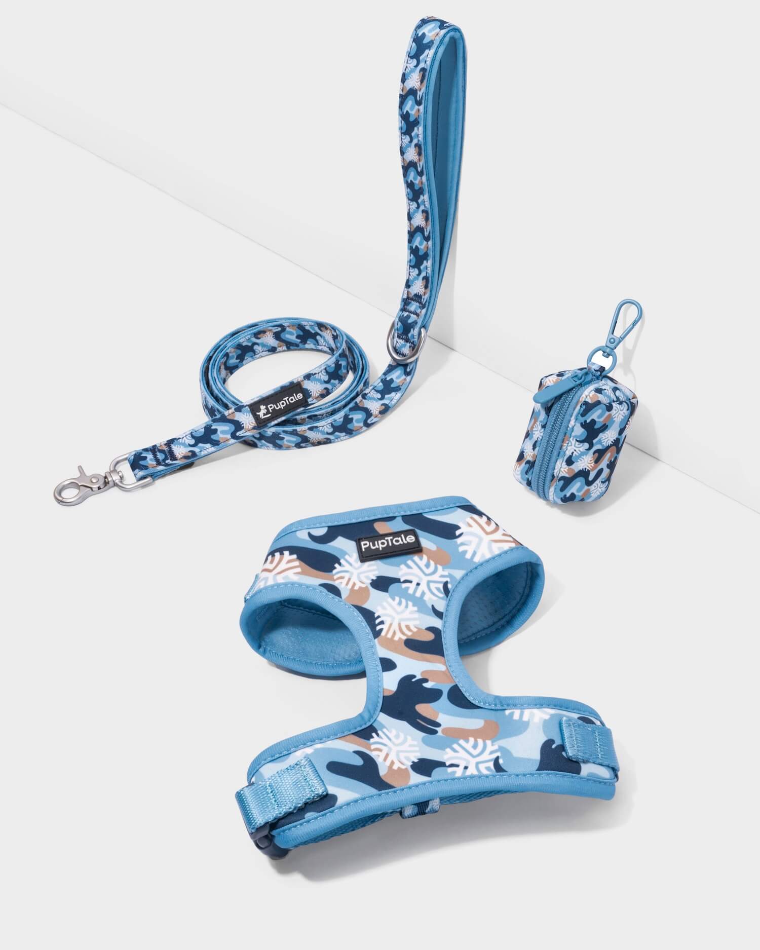 A set of puppy harness and leash with a snowflake pattern in blue and orange colors, displayed alongside a popp bag holder with a snowflake design.